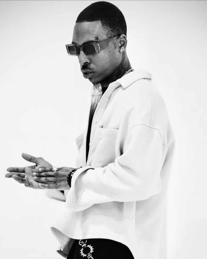 KamAllMighty in sunglasses and a cream overshirt